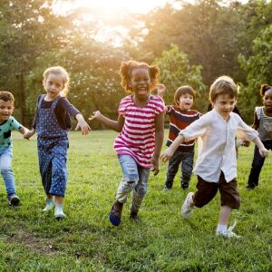 Children joyfully running on grass in a park, with sunlight filtering through trees in the background.